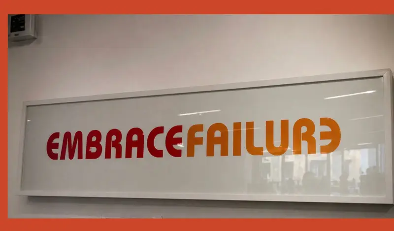 Framed 'Embrace Failure' sign on an office wall in red and orange lettering