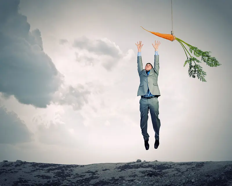 Businessman in a suit leaping for a carrot dangling on a string above him