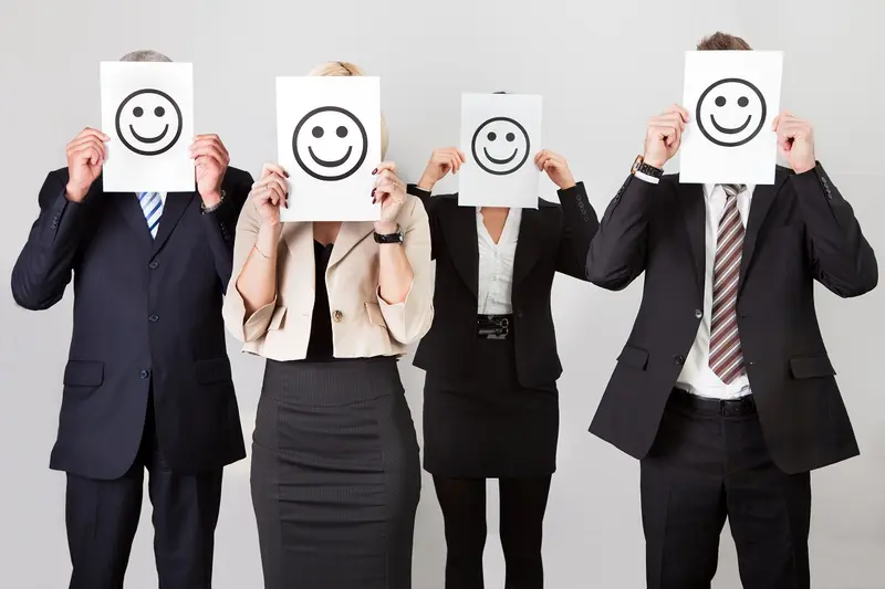 Four office workers in suits holding smiley-face signs over their faces