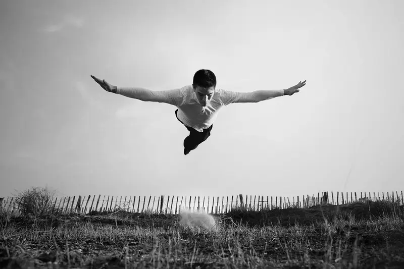 Black and white photo of a man leaping horizontally through the air, arms outstretched like a superhero in flight