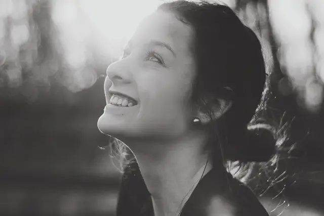 Black and white photo of a young woman smiling up toward the sunlight