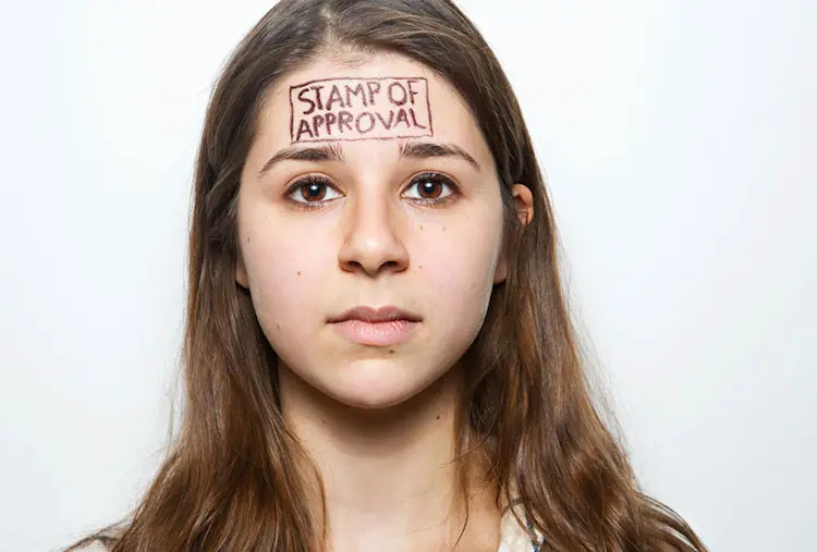 Young woman looking at the camera with “Stamp of approval” written on her forehead