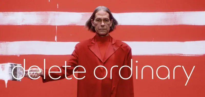 Stern man in a red suit painting white stripes on a red wall, captioned 'delete ordinary'