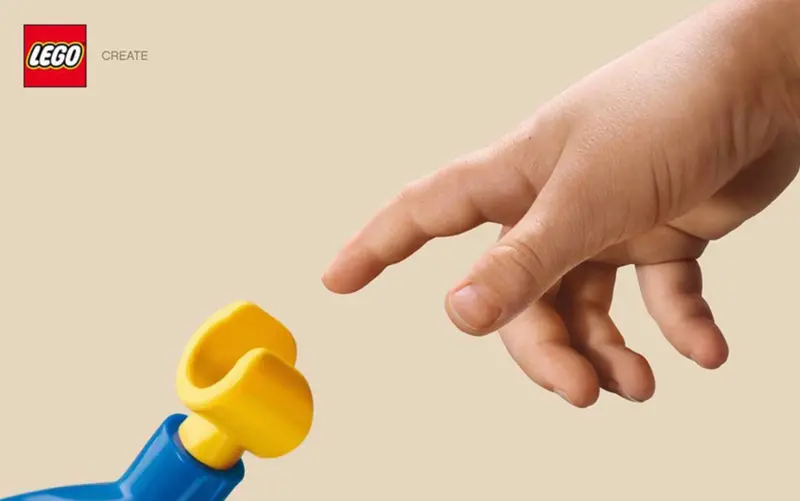 A human hand reaches towards the yellow hand of a LEGO minifigure, recreating Michelangelo’s Creation of Adam and illustrating how LEGO transforms simple plastic toys into creativity, imagination and emotional connection.